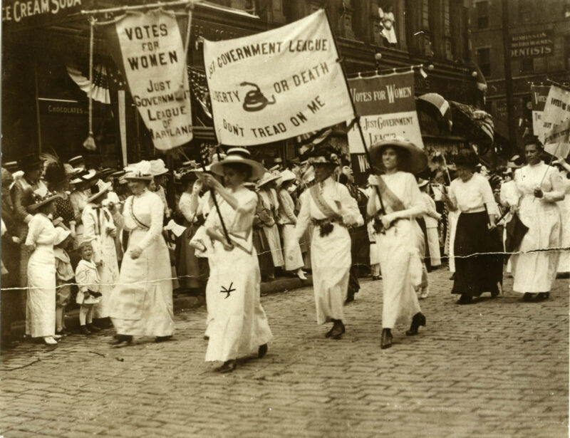 Black and white photo of women marching with large banners