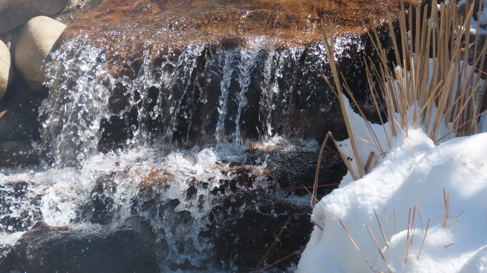 Photo of a running stream with snow on the bank