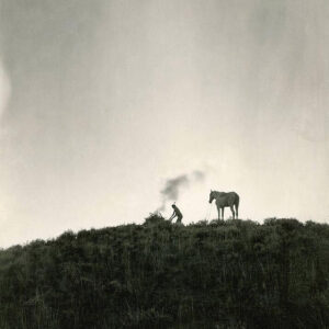 Black and white photo of Indian making smoke signals next to horse