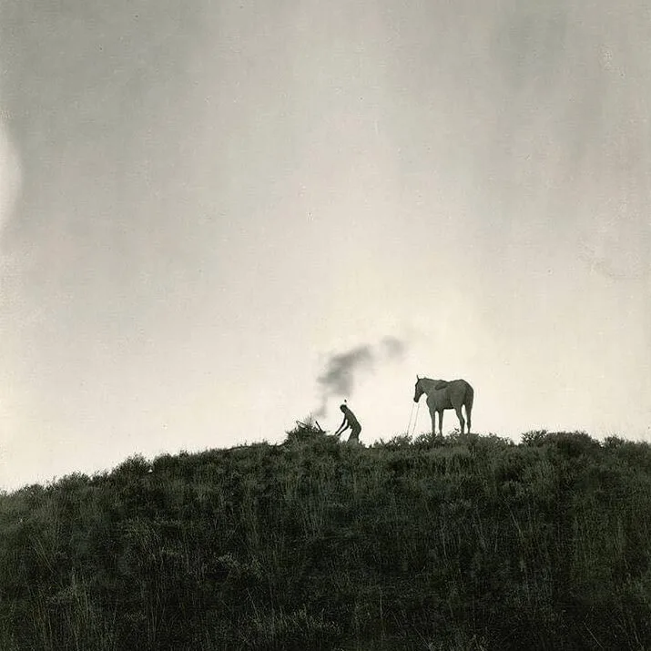 Black and white photo of Indian making smoke signals next to horse