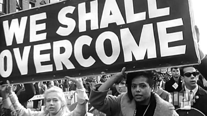 White and Black women holding up We Shall Overcome sign