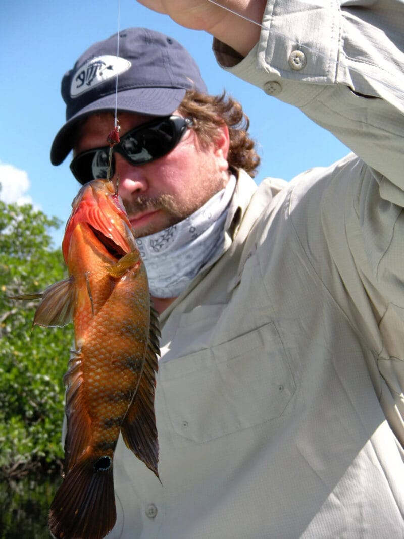 Photograph of man holding a fish on fishing line.