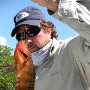 Photograph of man holding a fish on fishing line.